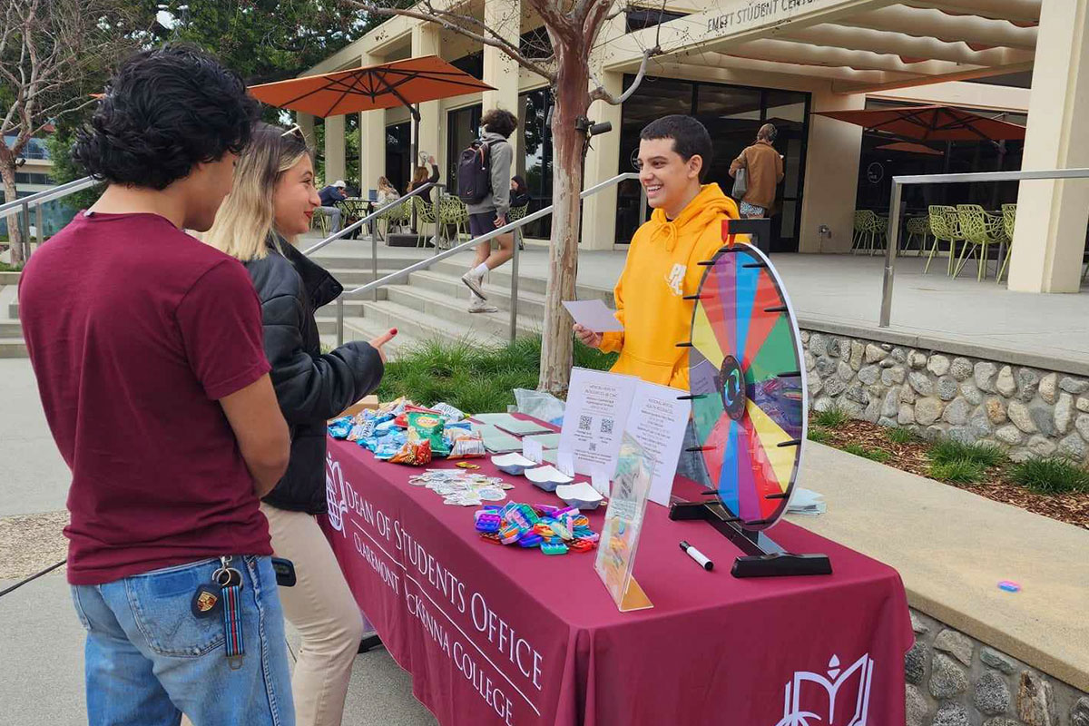 A Peer Health Ambassador hosting a table and speaking to two students.