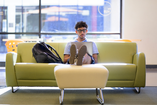 Male student sitting with his laptop in the Hub.