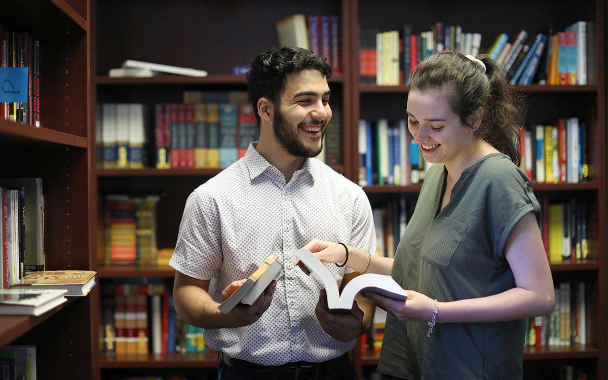 Two happy students holding books in a library.