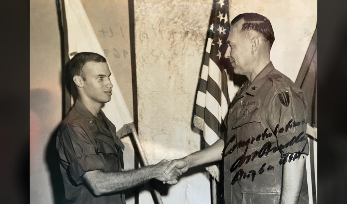 A signed black and white photo of Philip Chrones '66 in uniform shakes hands with a military senior.