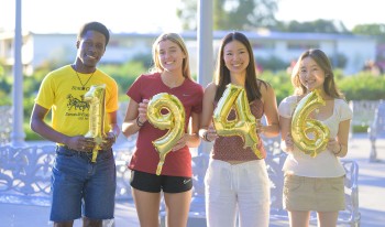 CMC students hold up gold mylar balloons reading &quot;1946.&quot;