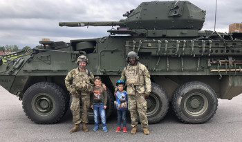 Ash and his friend stand with two children in front of a tank.