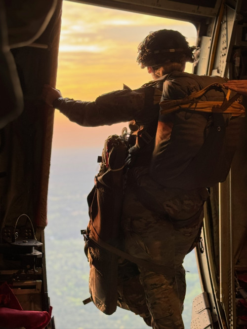 Lauren Jeans '24 stands at an open door of an airborne helicopter, looking out into a colorful sunset.