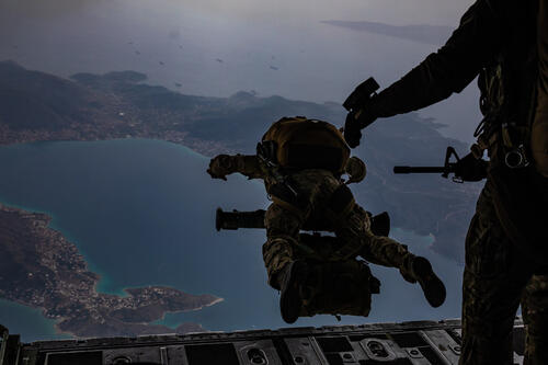 Military men jumping off plane into ocean wearing uniform.