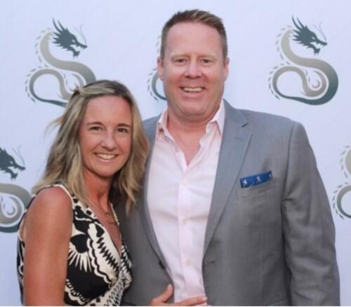 Man and woman in dressy clothes in front of photo op hugging. 