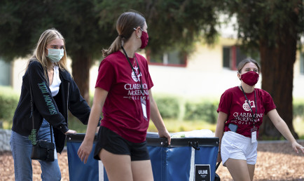 Two students in red CMC t-shirts roll a wheeled cart together to help another student on her move-in day