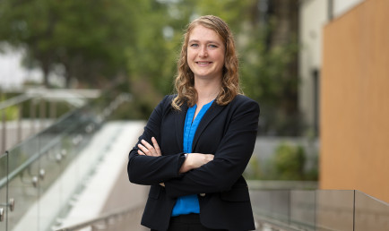 Professor Sarah Cannon poses with a smile and crossed arms on campus