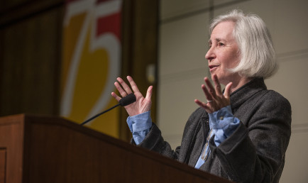 Martha Minow addresses attendees from the Ath podium. Behind her hangs a 75th Anniversary banner.