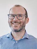 Man smiling wearing a blue shirt and glasses.