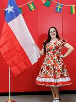 Woman with long black hair wearing red floral dress holding Chile flag. 